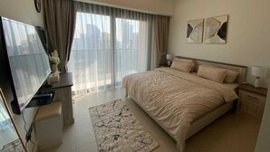 Ein Schlafzimmer mit einem großen Bett, einem Fernseher, einem Schreibtisch und einem Fenster mit Vorhängen.