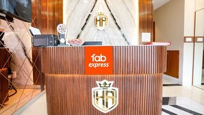 Un comptoir d’accueil d’hôtel avec un revêtement en bois, une enseigne indiquant « fab express » et un logo représentant une couronne et les initiales « HA ».