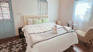 A bedroom with a bed, a chair, a small table, and a window with curtains. - La Address Retreat (Ootacamund)