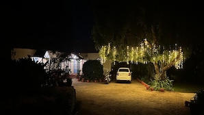 A white car parked in front of a building with string lights hanging from a tree. - La Address Retreat (Ootacamund)