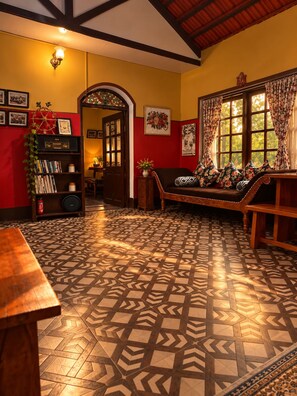 A room with a patterned floor, a wooden bench, a bookshelf, and a door leading to another room. - La Address Retreat (Ootacamund)