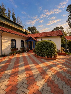 A courtyard with a red-tiled roof, a white building with arched windows, and a well-maintained hedge. - La Address Retreat (Ootacamund)