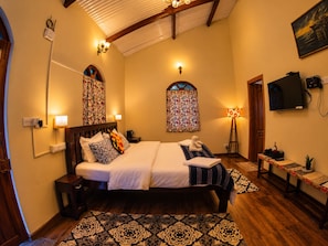 A hotel room with a large bed, two bedside tables, a TV, and a window with curtains. - La Address Retreat (Ootacamund)