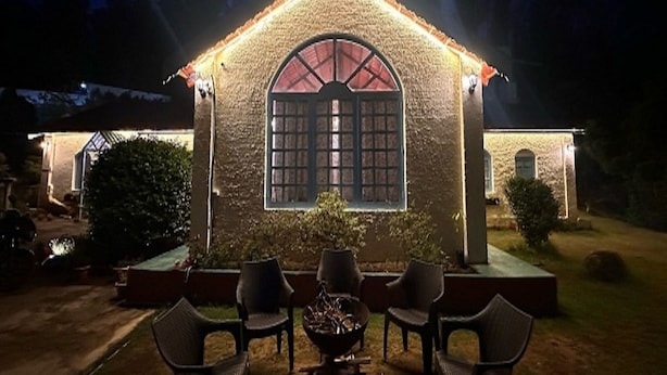 A stone building with a large arched window and a small patio with chairs and a table. - La Address Retreat (Ootacamund)