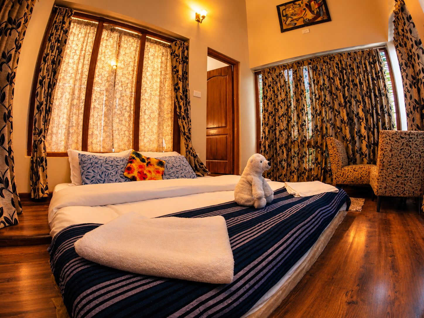 A hotel room with a bed, a chair, and a teddy bear.