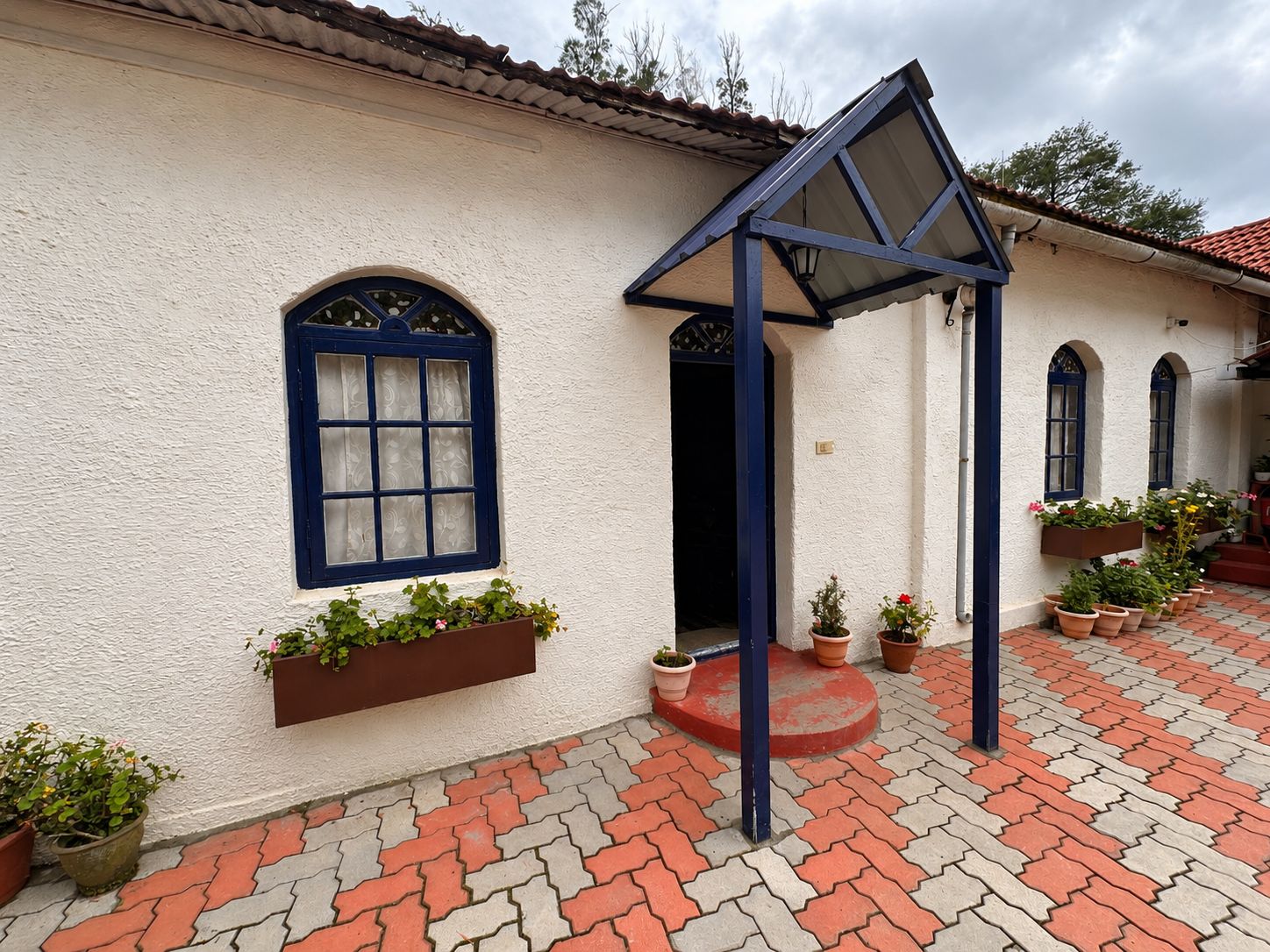 Un edificio con fachada blanca, marcos de ventana azules y un patio con pavimento de baldosas.