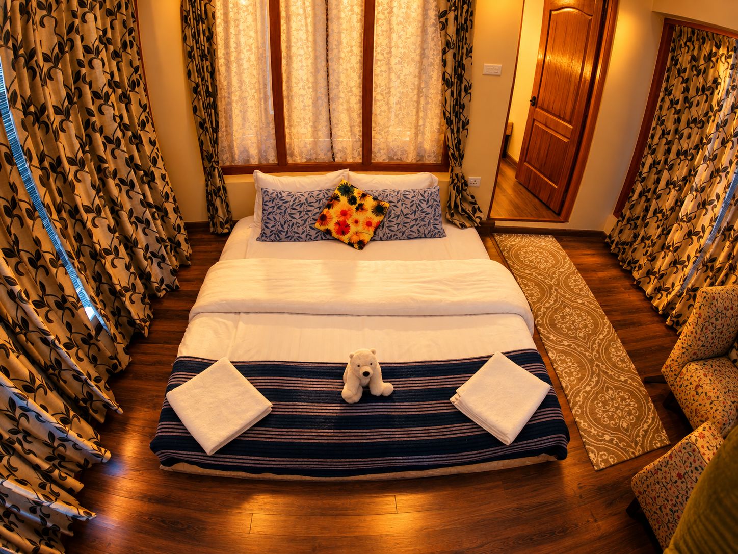 A hotel room with a large bed, a bedside table, a chair, and curtains with a leaf pattern.