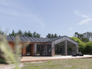 Et moderne hus med skråt tag, store glasruder og en træterrasse.