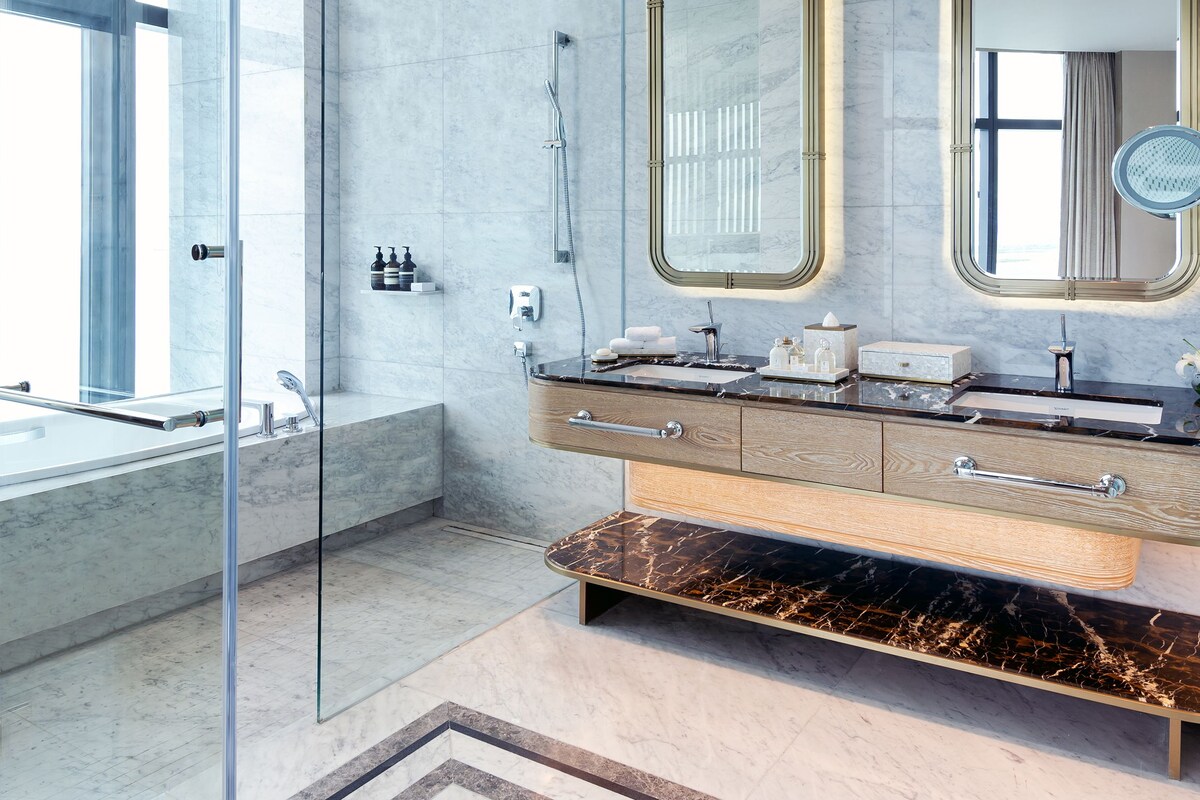 A modern bathroom with a glass shower enclosure, a large vanity with a mirror, and a marble floor.