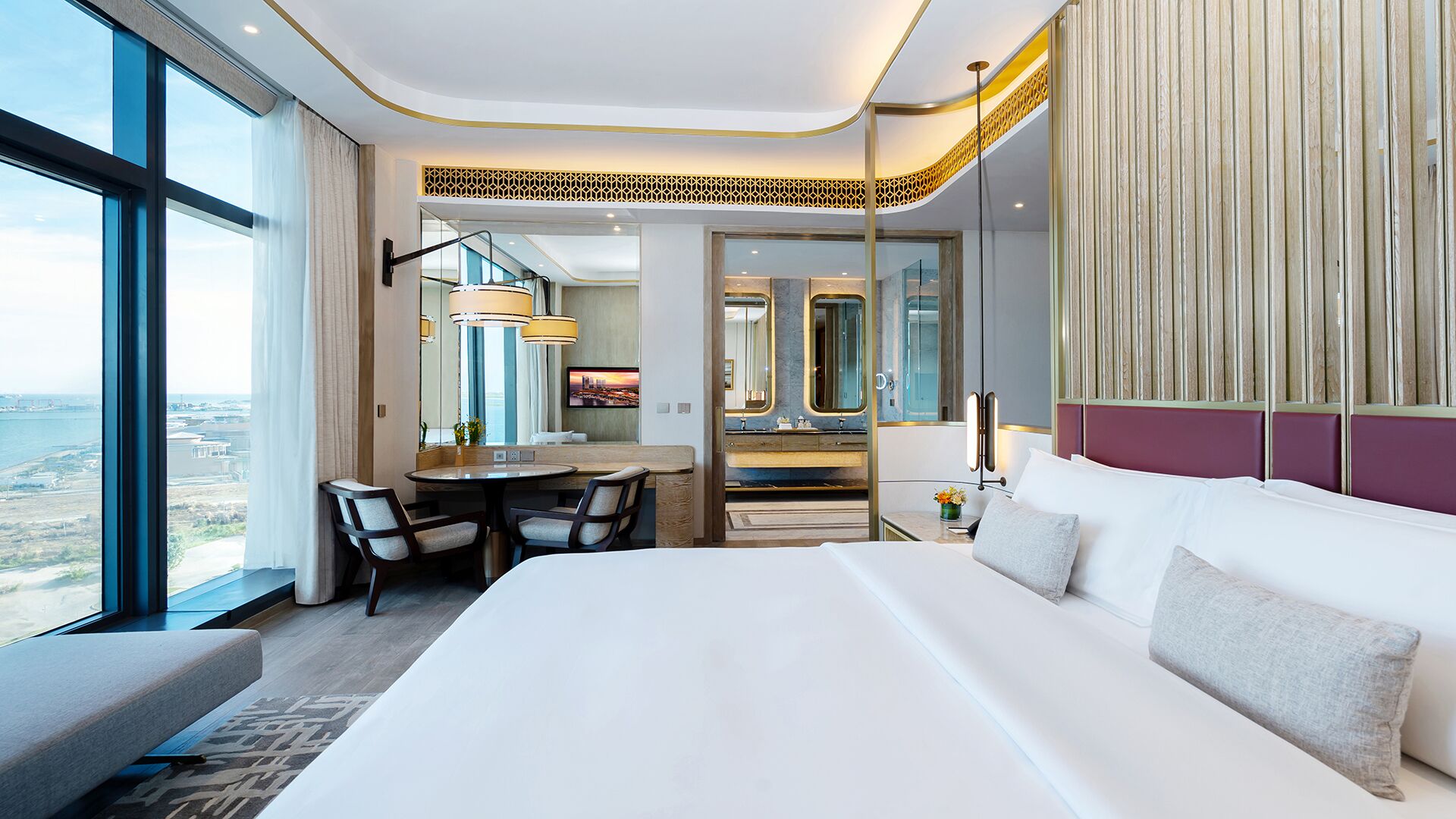 A hotel room with a large bed, a desk, a chair, a vanity with a mirror, and a view of the city.