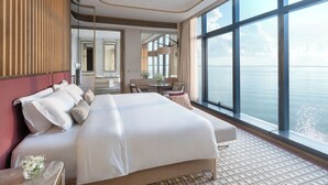 A spacious bedroom with a large bed, a sitting area, a view of the sea, and a mirror reflecting the room. - NUSTAR Hotel Cebu (Cebu City)