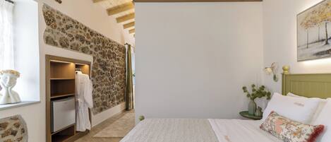 Un dormitorio con pared de piedra, vigas de madera en el techo, una cama con ropa de cama blanca y una mesita de noche con un jarrón.