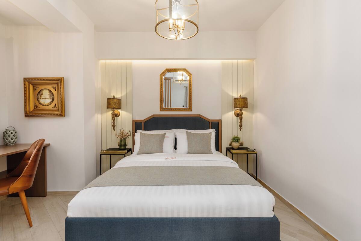 A hotel room with a large bed, bedside tables, a desk, and a chair.