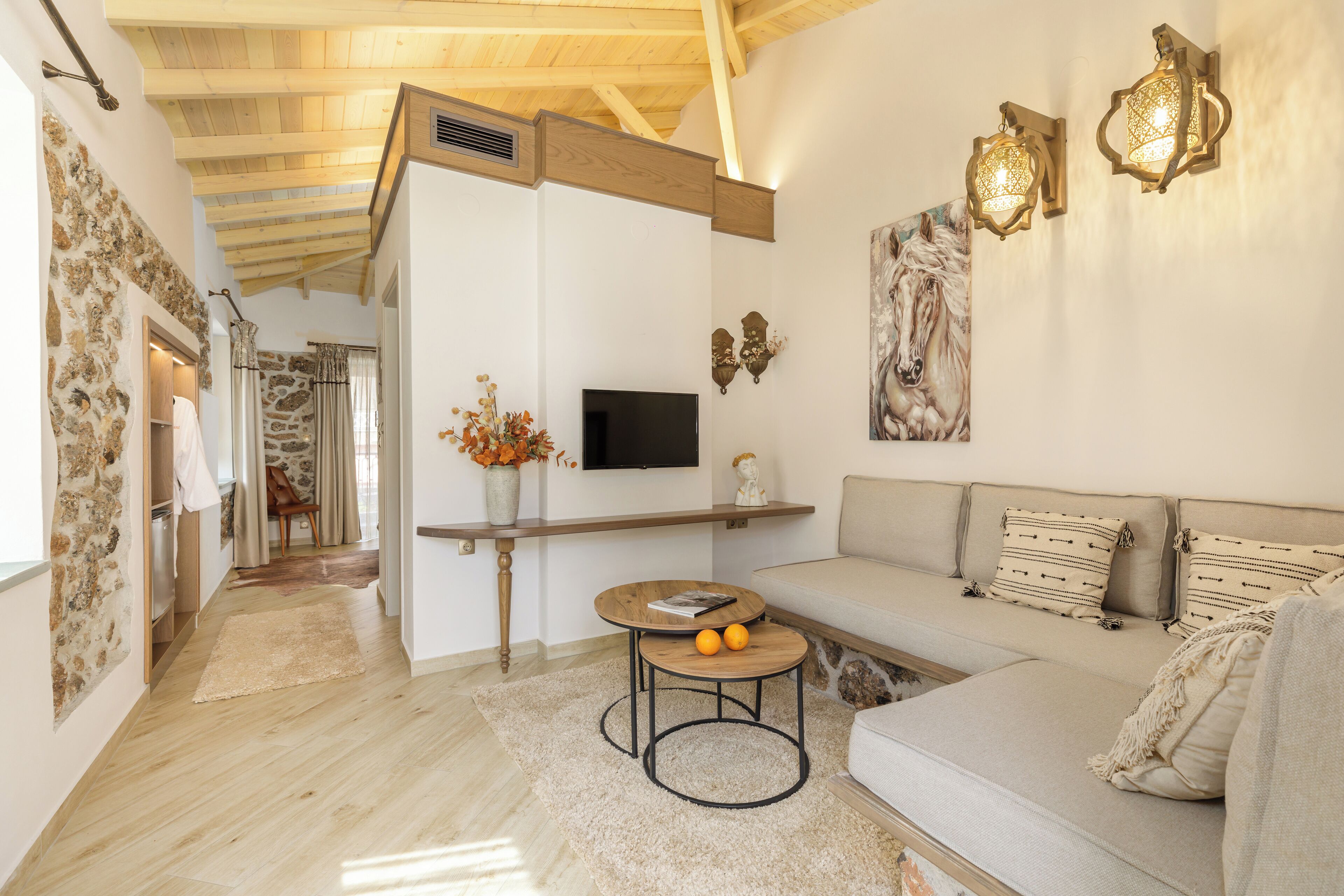 Een moderne woonkamer met een houten plafond, een stenen muur, een bank, een salontafel met sinaasappels, en een flatscreen-televisie.