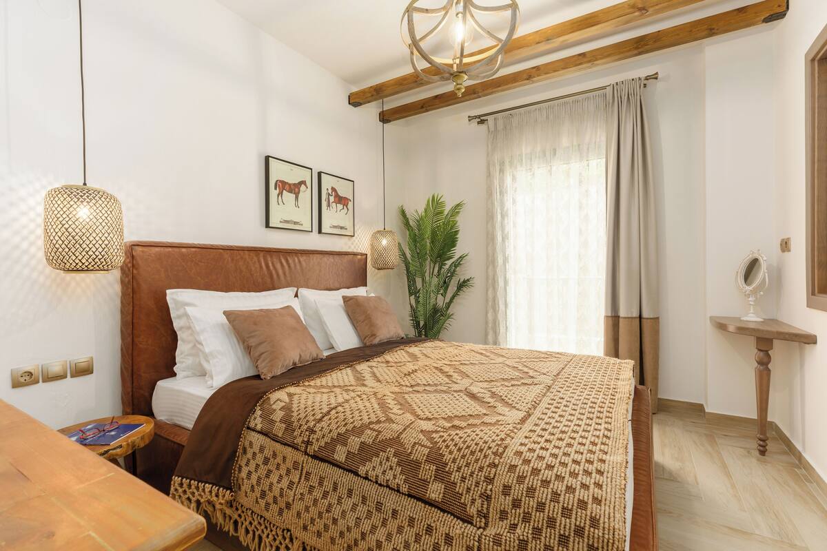 A bedroom with a wooden headboard, a patterned bedspread, a bedside table with glasses, and a hanging light fixture.