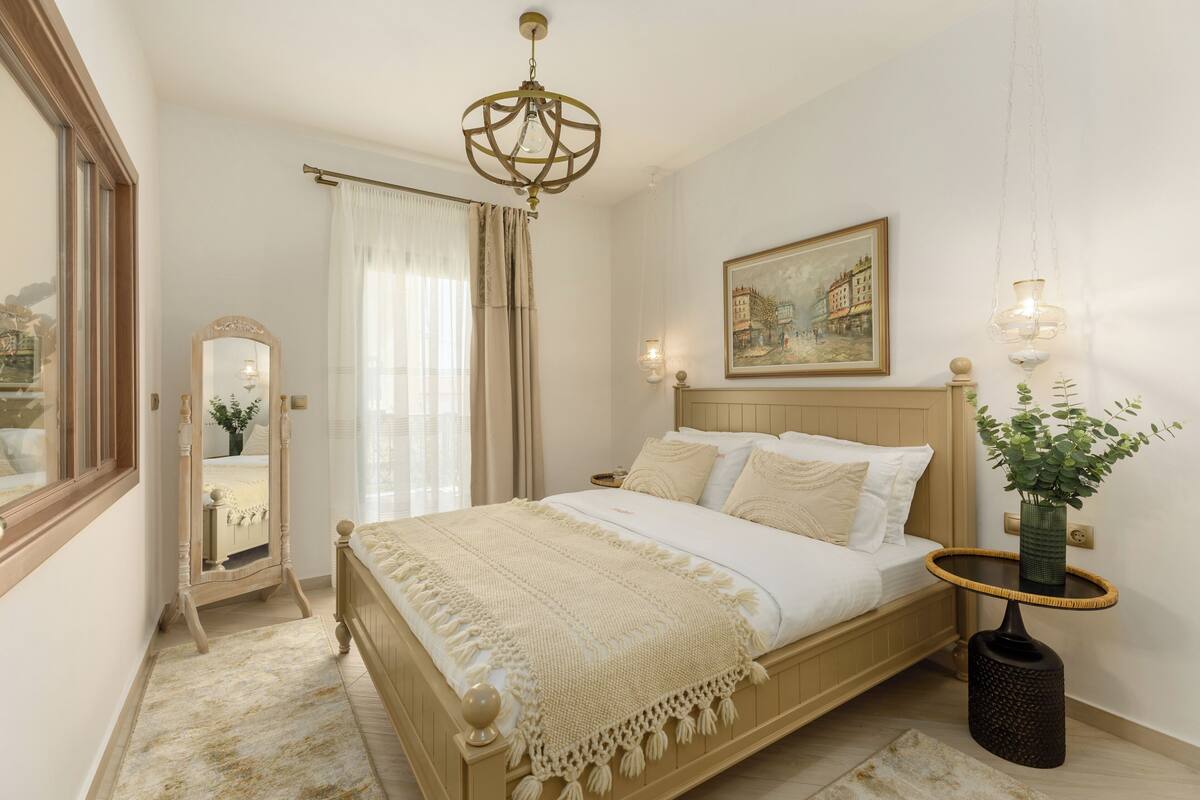 A bedroom with a wooden bed, a mirror, a painting, and a hanging plant.