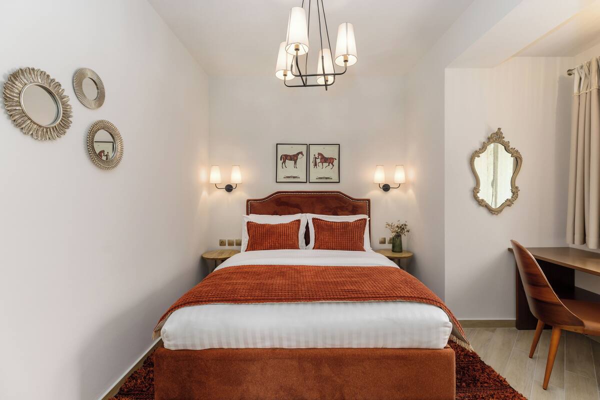 A bedroom with a large bed, a wooden headboard, two wall-mounted lamps, a mirror, and a desk with a chair.
