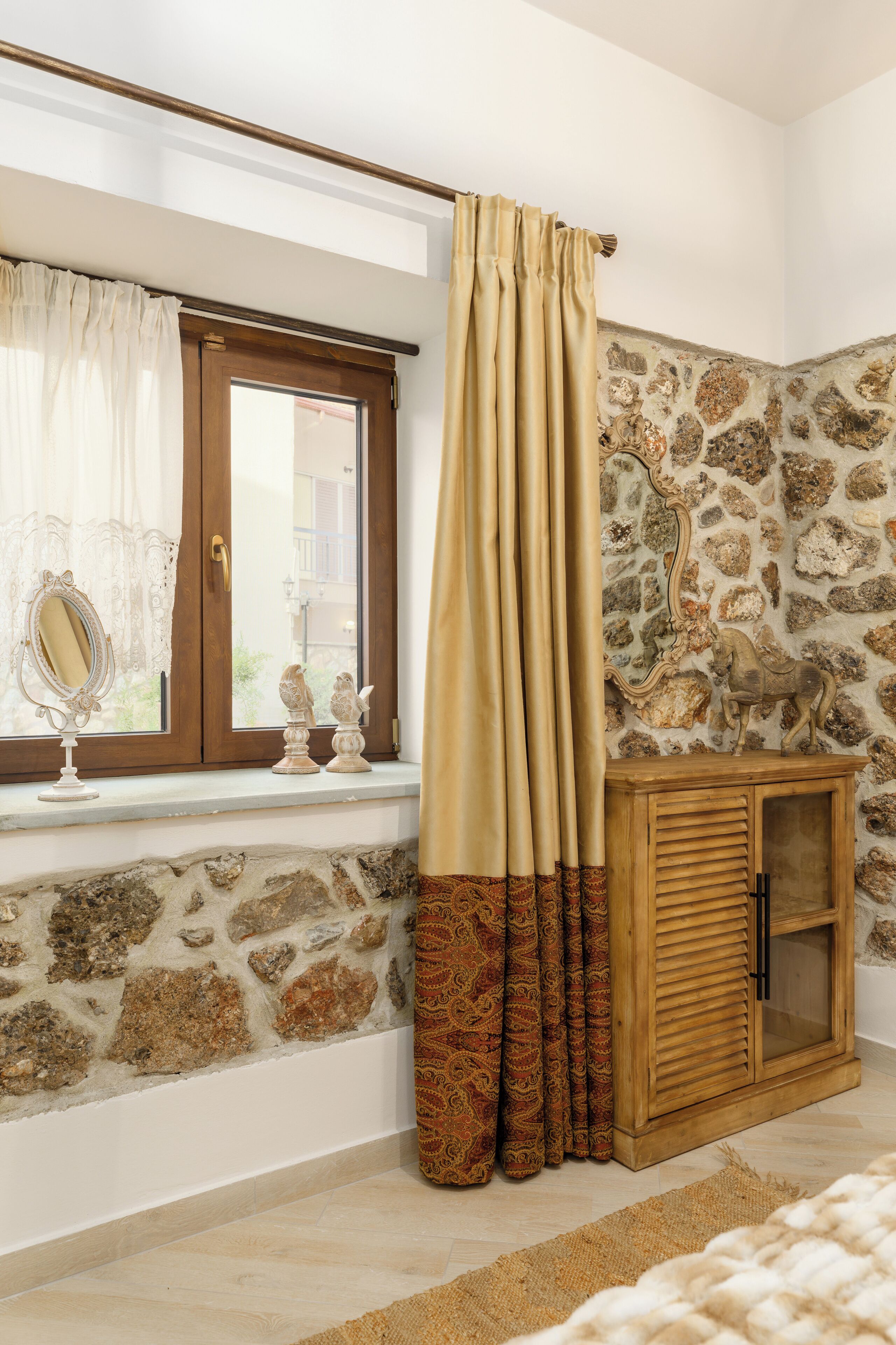 Una habitación con pared de piedra, un armario de madera y una ventana con cortinas.