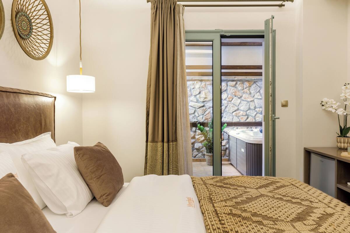 A bedroom with a bed, pillows, a bedside lamp, a curtain, and a view of a balcony with a stone wall and a sink.
