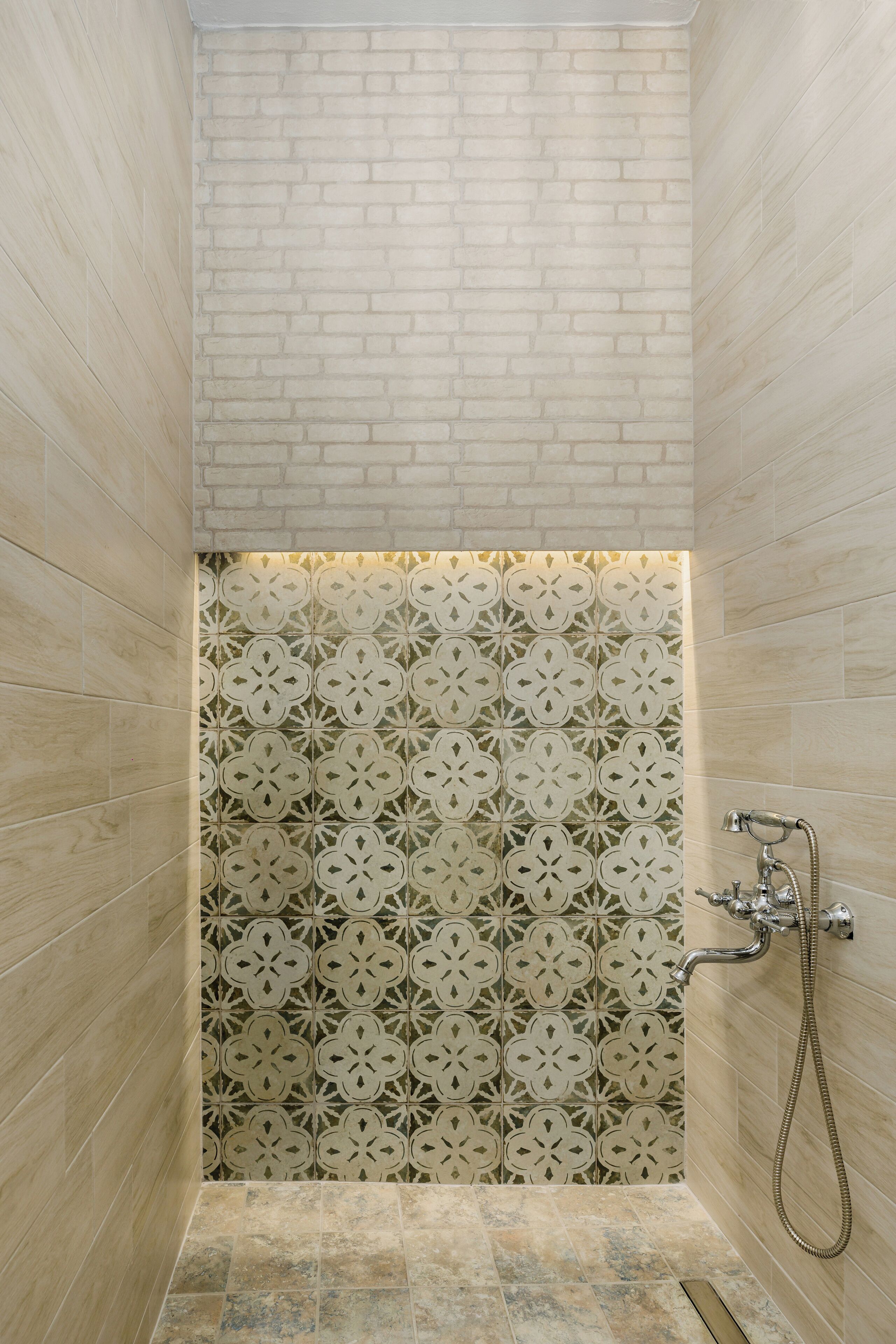 A shower with a patterned tile wall, a visible showerhead, and a drain.