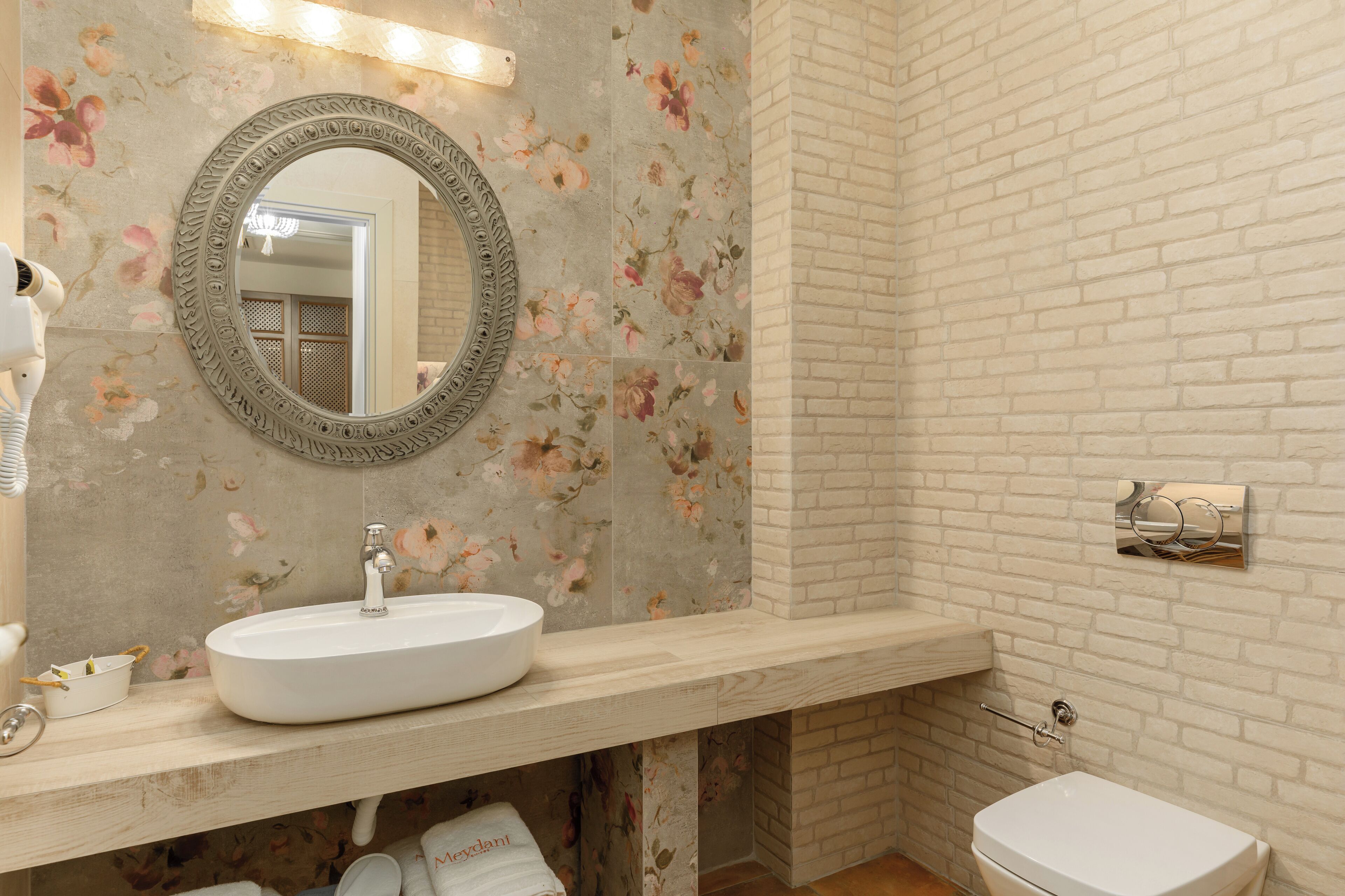 A bathroom with a floral-patterned wall, a round mirror, a white sink, and a white toilet.