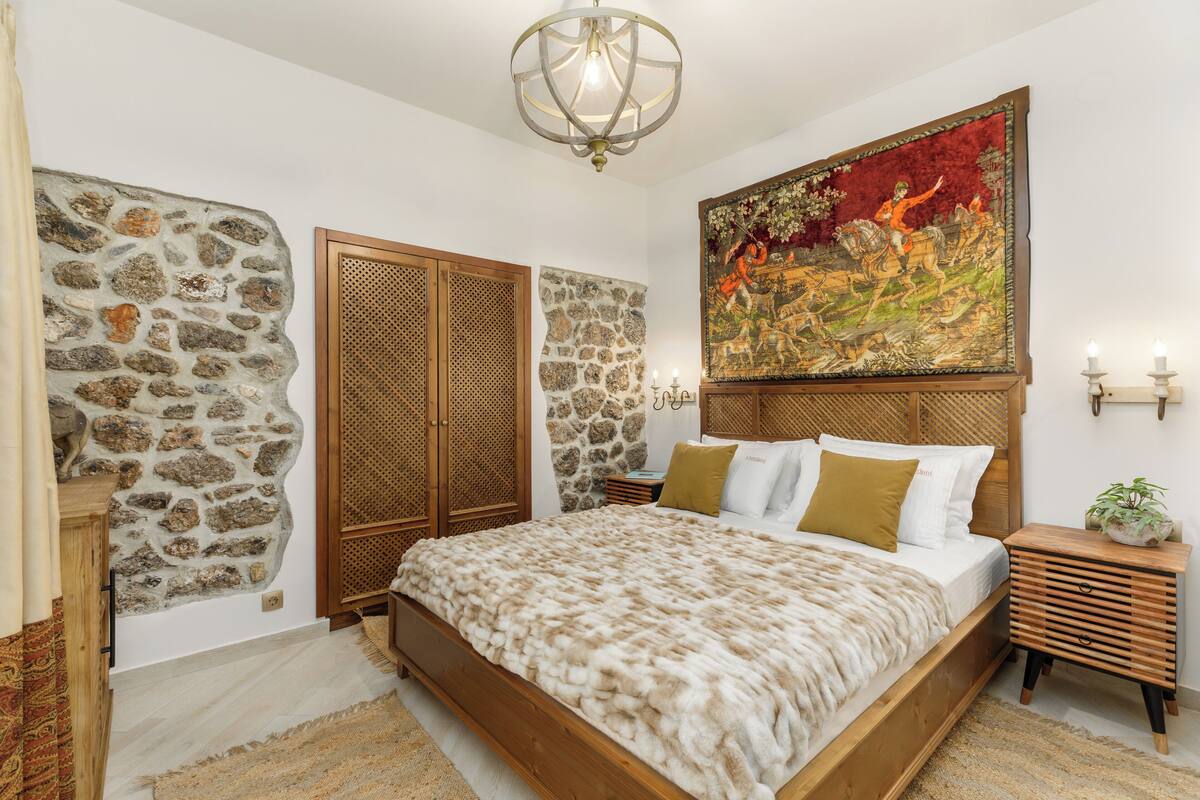 A bedroom with a stone wall, a large painting, a wooden bed, and a nightstand with a plant.