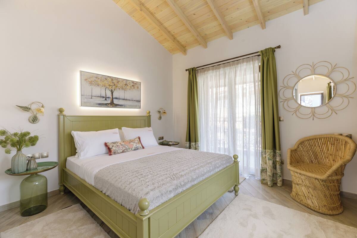 A bedroom with a green bed, a wicker chair, a mirror, and a painting on the wall.