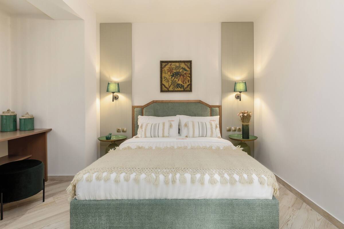 A neatly arranged bedroom with a large bed, two bedside tables, a nightstand, a desk, and a chair.