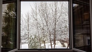 A window with a view of snow-covered trees and a building in the background. - Rustic Modern Studio • Ski-in, Ski-out • King Bed (Wengen)
