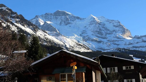A mountain lodge with a wooden exterior, a visible sign, and a view of snow-covered peaks. - Rustic Modern Studio • Ski-in, Ski-out • King Bed (Wengen)