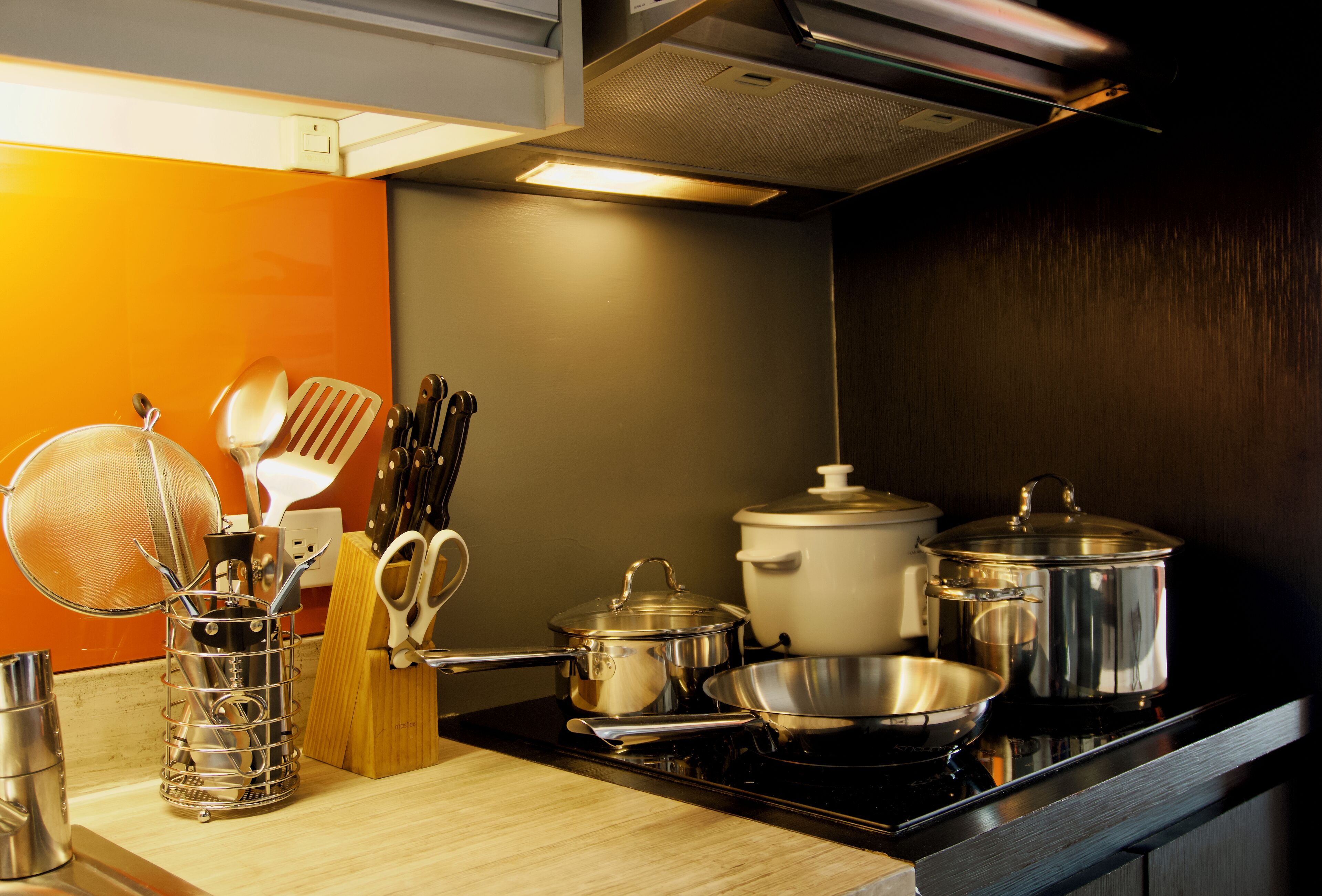 A kitchen with a stove, pots, pans, and utensils.