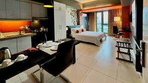 Ett modernt hotellrum med ett litet kök, en matplats, en stor säng och utsikt över staden.