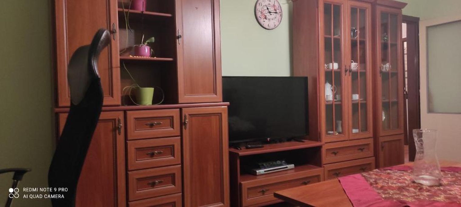 Un salon avec des meubles en bois, un téléviseur et une horloge au mur.