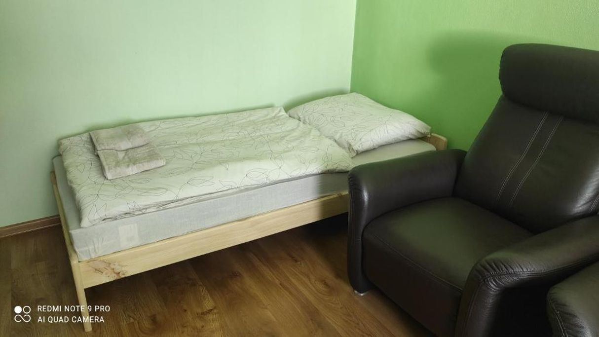 Una habitación con una cama, un sillón de cuero negro y una pared verde.