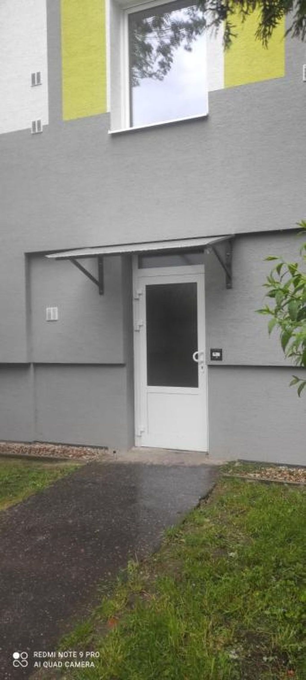 Ein Gebäudeeingang mit einer weißen Tür, einem kleinen Fenster darüber und einem Schild an der Wand.