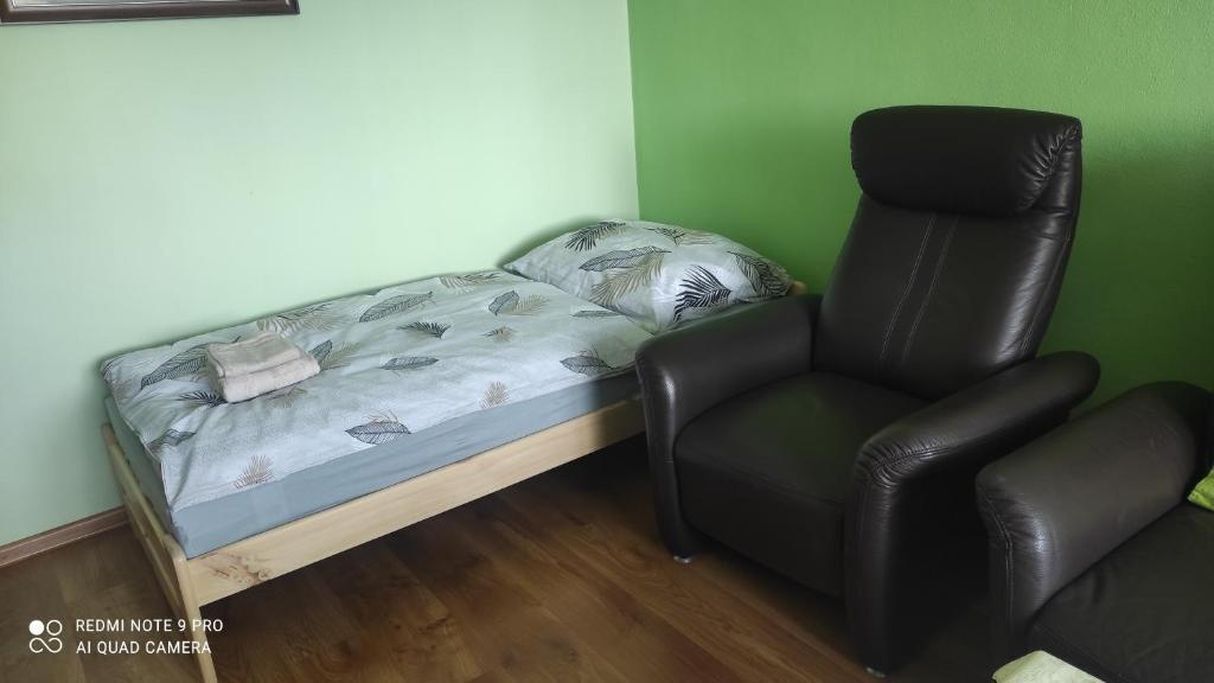 Una habitación con una cama, un sillón de cuero negro y una pared verde.