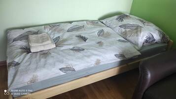 Uma cama de solteiro com colcha e almofadas estampadas com folhagens, cabeceira de madeira e uma cadeira de couro marrom.