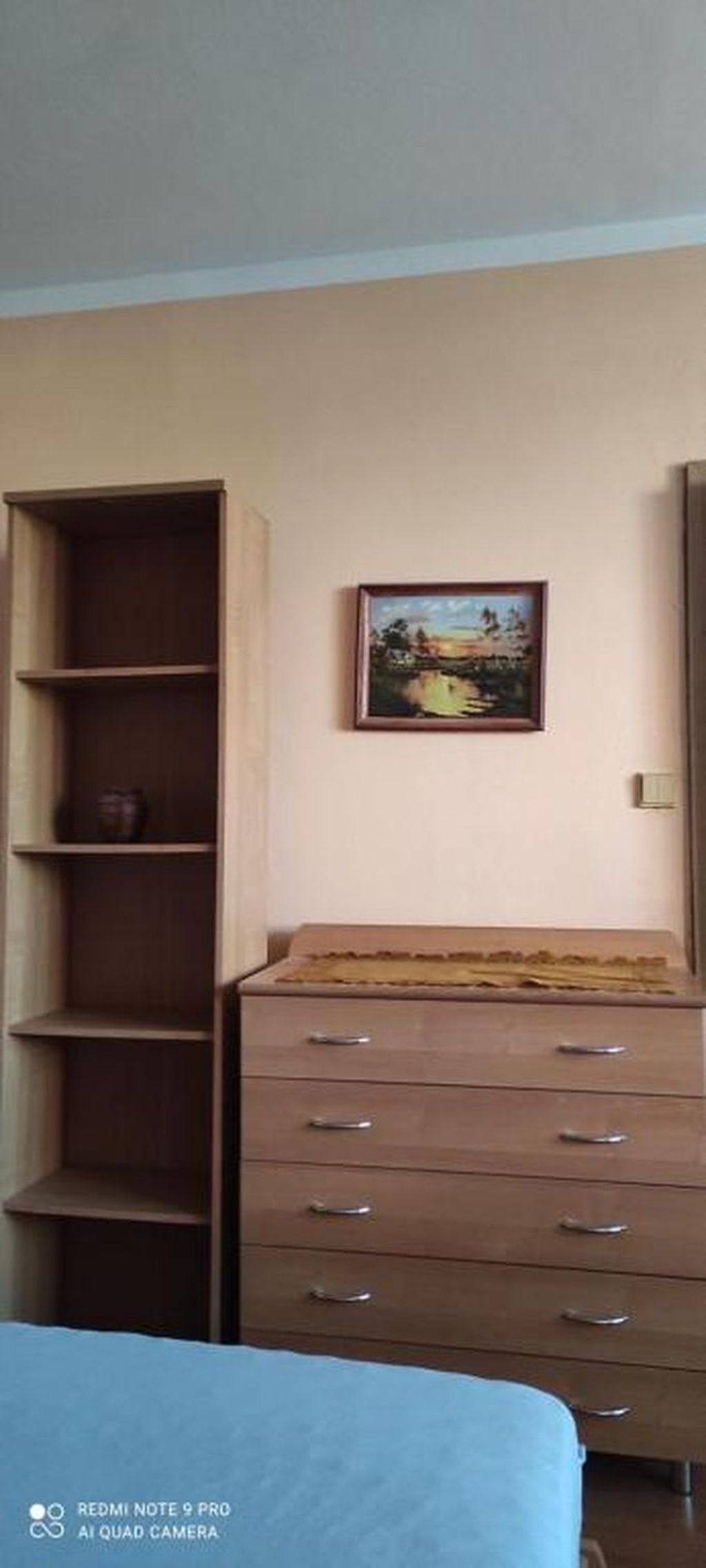 Une chambre à coucher comprenant un lit, une commode, une étagère et un tableau encadré accroché au mur.