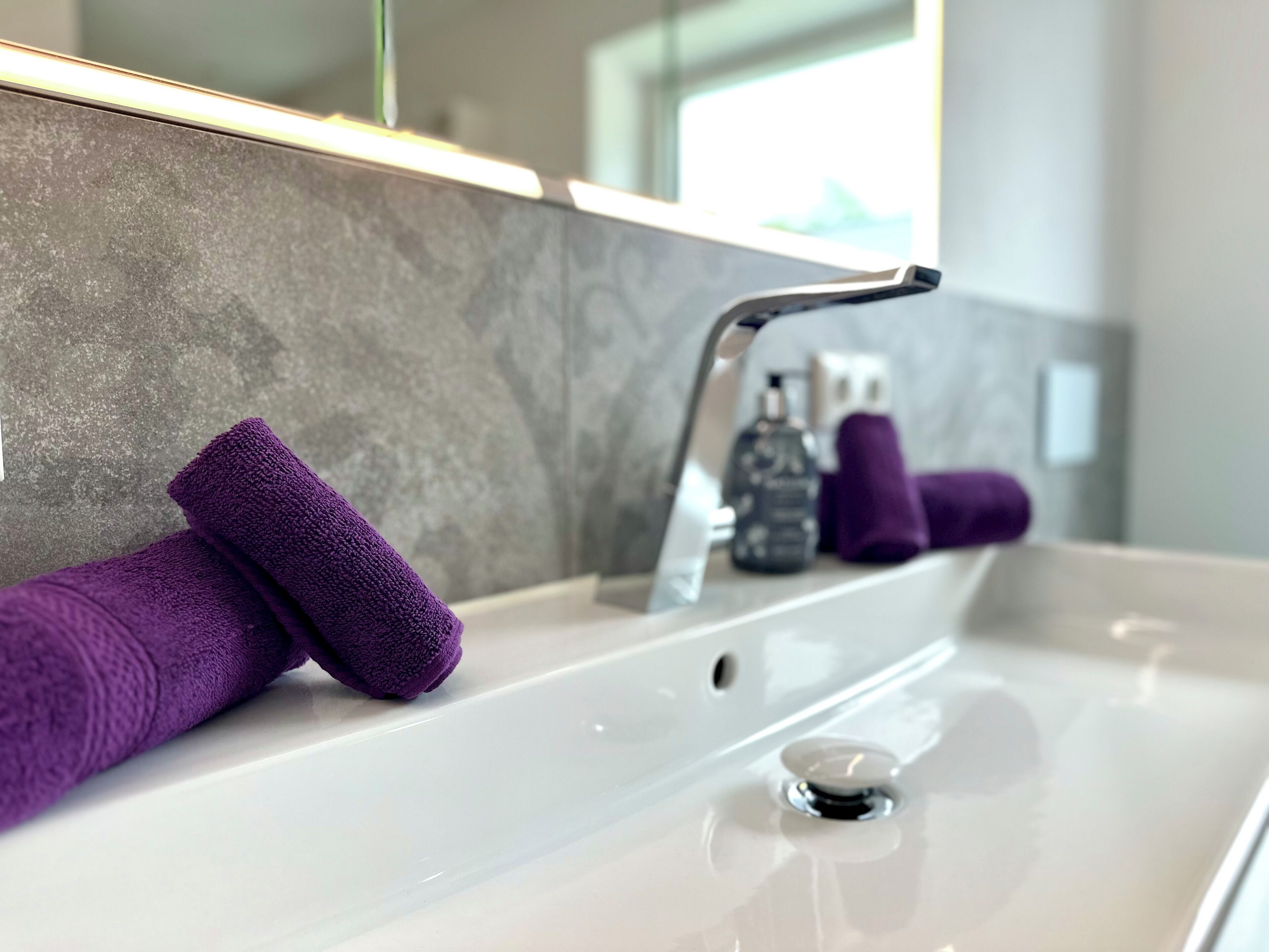Ein Badezimmer mit einem weißen Waschbecken, einem Spiegel und zwei lilafarbenen Handtüchern.