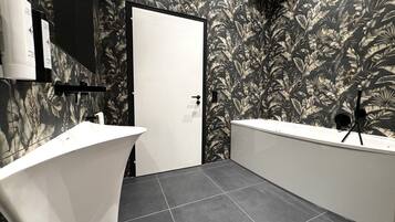 A modern bathroom with a white bathtub, a separate shower area, and a toilet. The walls are adorned with a tropical leaf pattern.