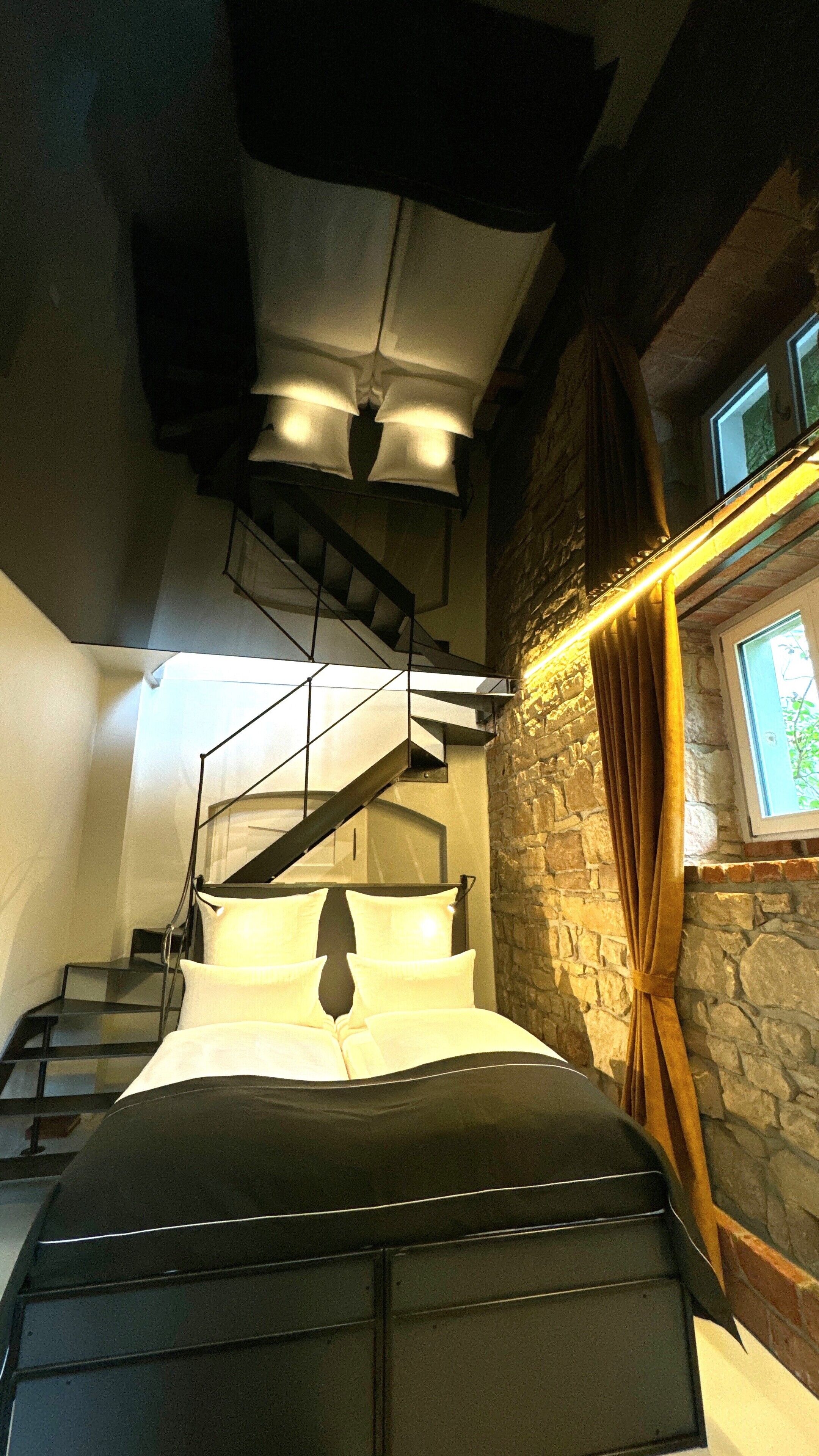 A bedroom with a bed, a staircase, and a stone wall.