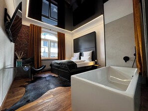 Un dormitorio moderno con una cama grande, un baño independiente con bañera, un ventanal con cortinas y una pared de ladrillo.