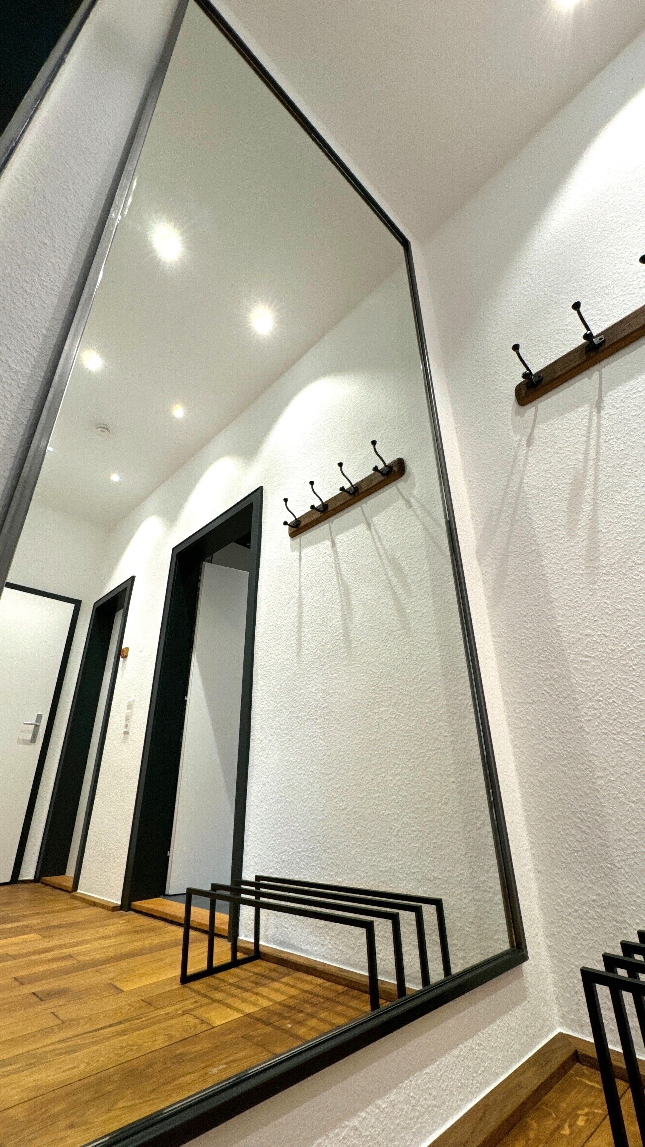 A modern hotel room with a large mirror, wooden flooring, and a coat rack.