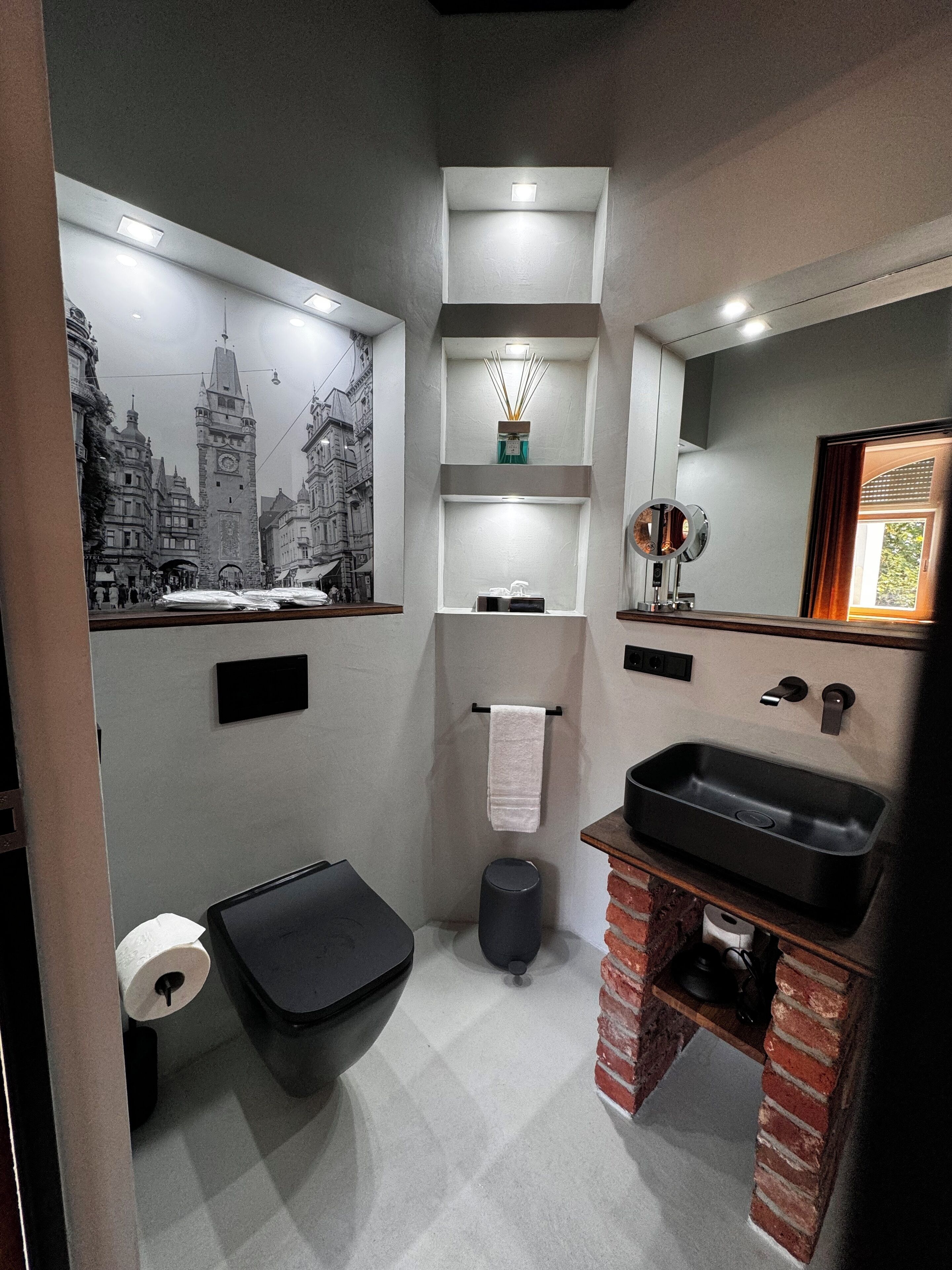 A modern bathroom with a black sink, a toilet, and a mirror. There is a towel hanging on a rack and a picture frame on the wall.