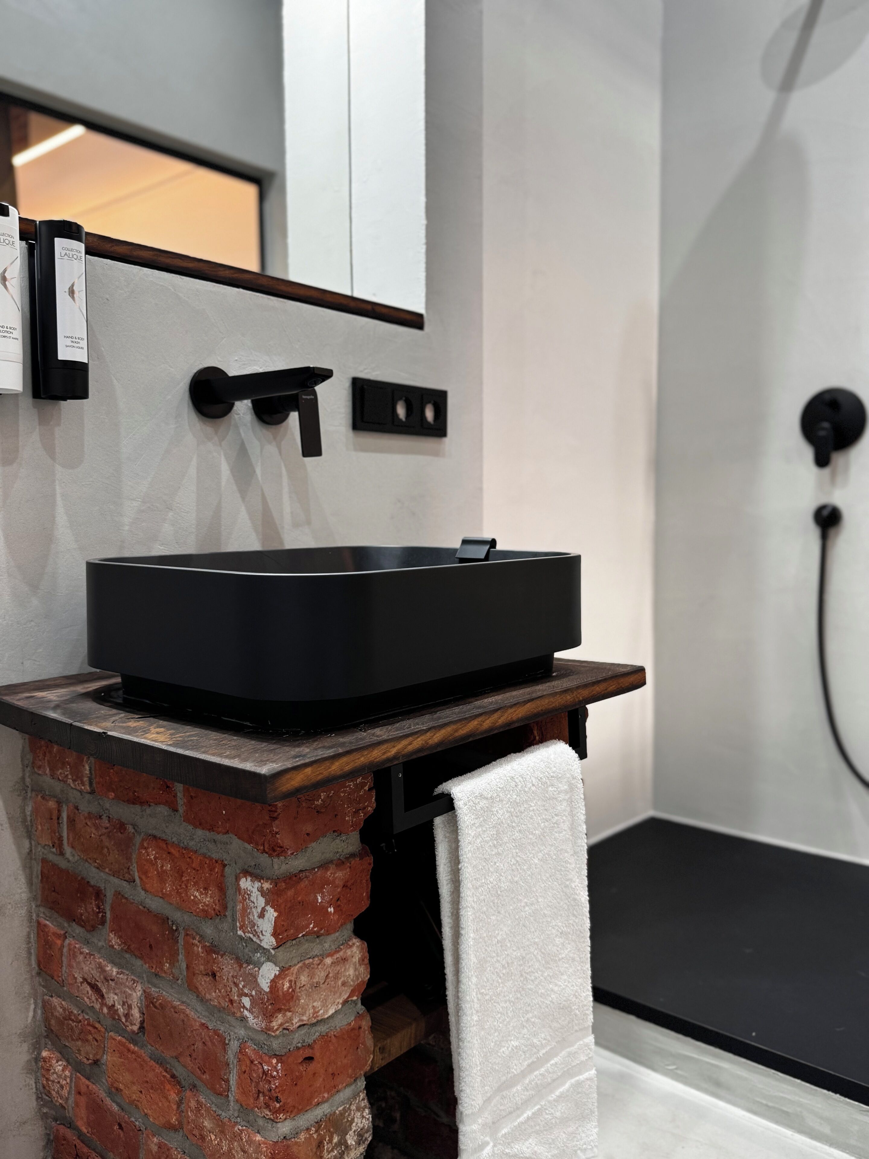A modern bathroom with a black bathtub, a wooden vanity, and a brick accent wall.