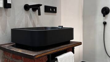 A modern bathroom with a black bathtub, a wooden vanity, and a brick accent wall.
