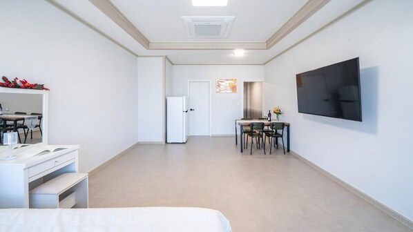 A hotel room with a bed, a desk with a chair, a dining table with chairs, a TV mounted on the wall, and a white door. - Yeosu Wayo Ocean View Pension (Yeosu)