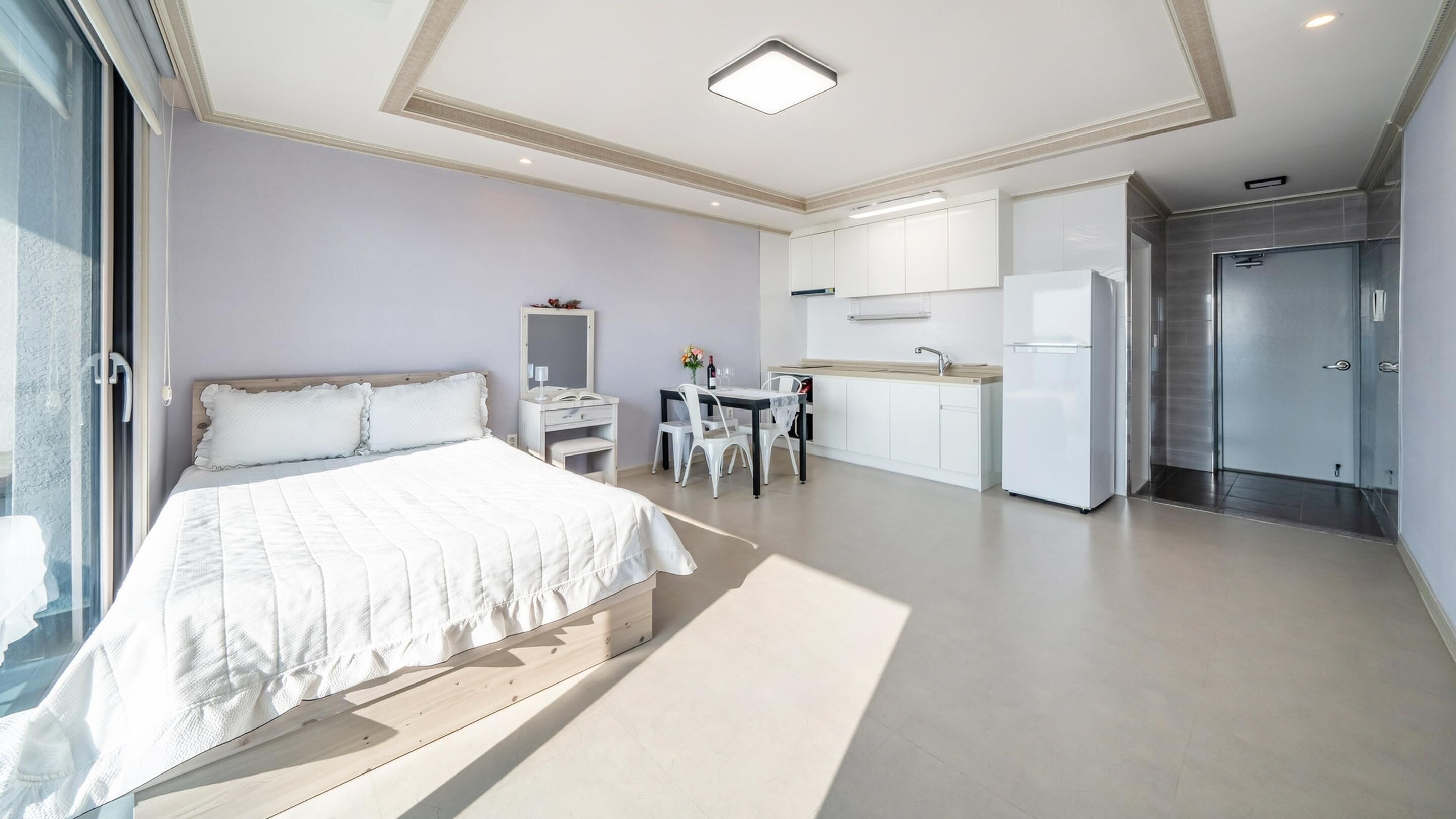 A modern bedroom with a large bed, a desk, and a kitchenette.