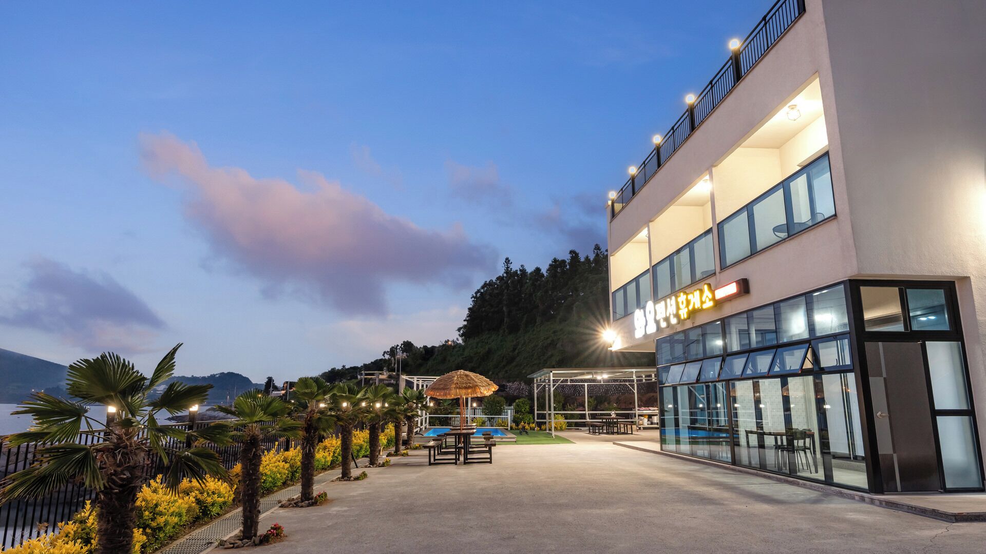 A modern hotel with a pool area, outdoor seating, and a view of the mountains.