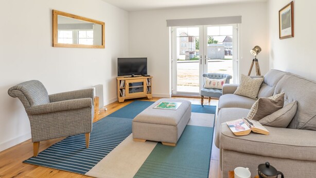 Een woonkamer met een bank, fauteuil, pouf en een televisie op een houten dressoir.